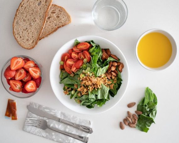Top view of a healthy salad and fresh ingredients with bread and juice on a white surface.