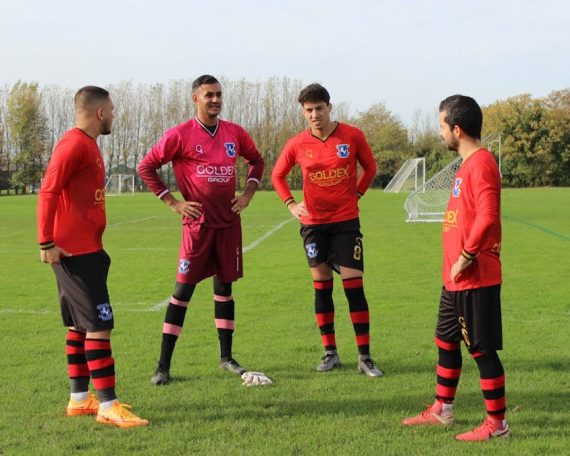 Four soccer players in red and black uniforms strategizing on a green football field.